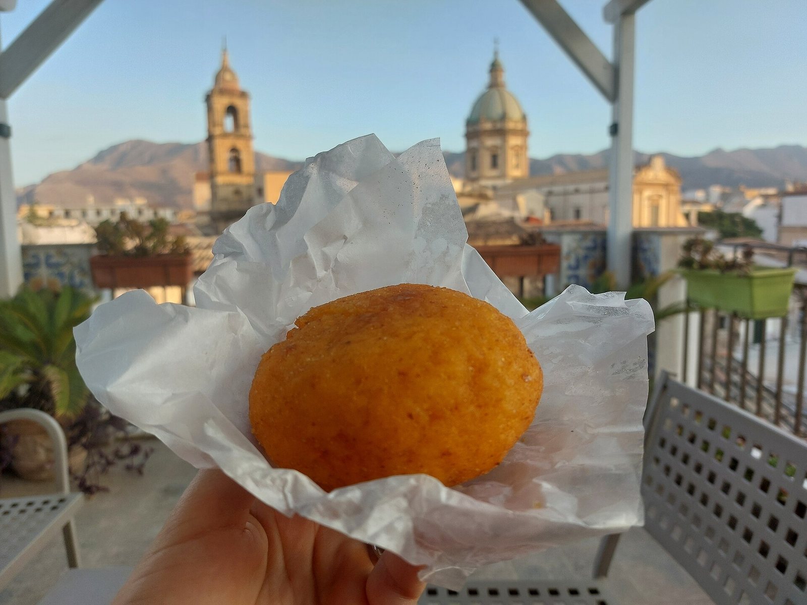 Arancina siciliana avvolta nella carta, con i campanili di Palermo sullo sfondo